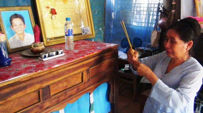 Bà Mai rưng rưng nước mắt thắp nén nhang bên di ảnh chồng - Ảnh: Sơn Bình