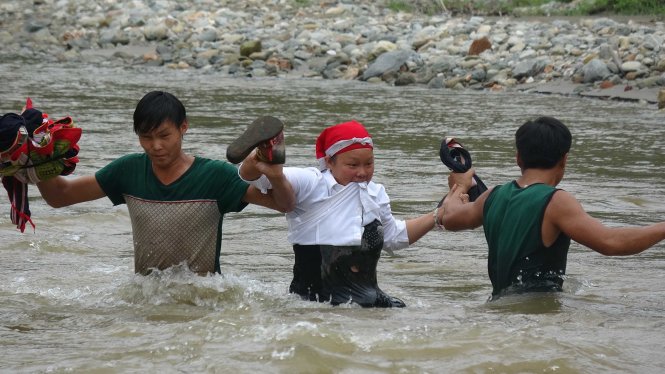 Một người phụ nữ được hai thanh niên “hộ tống” qua dòng nước lũ - Ảnh: Chí Tuệ