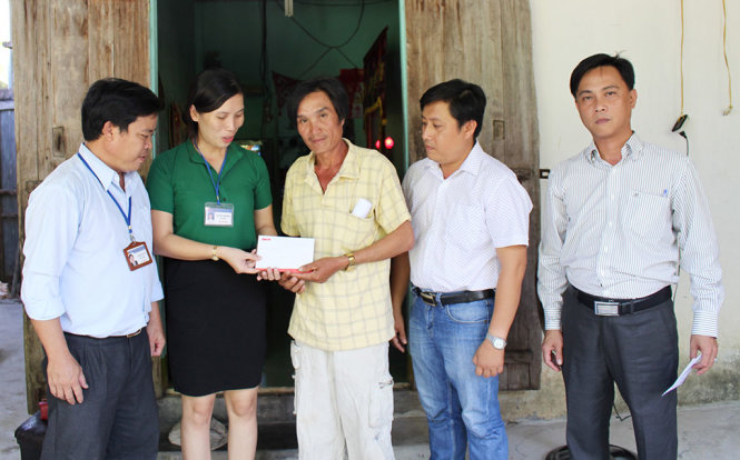 Bà Nguyễn Thị Thanh Hương, chủ tịch UBND thị trấn Củng Sơn, trao tiền hỗ trợ của bạn đọc báo Tuổi Trẻ cho ông Phạm Xuân Hoàng, cha em Phạm Xuân Luật - Ảnh: TRUNG HIẾU