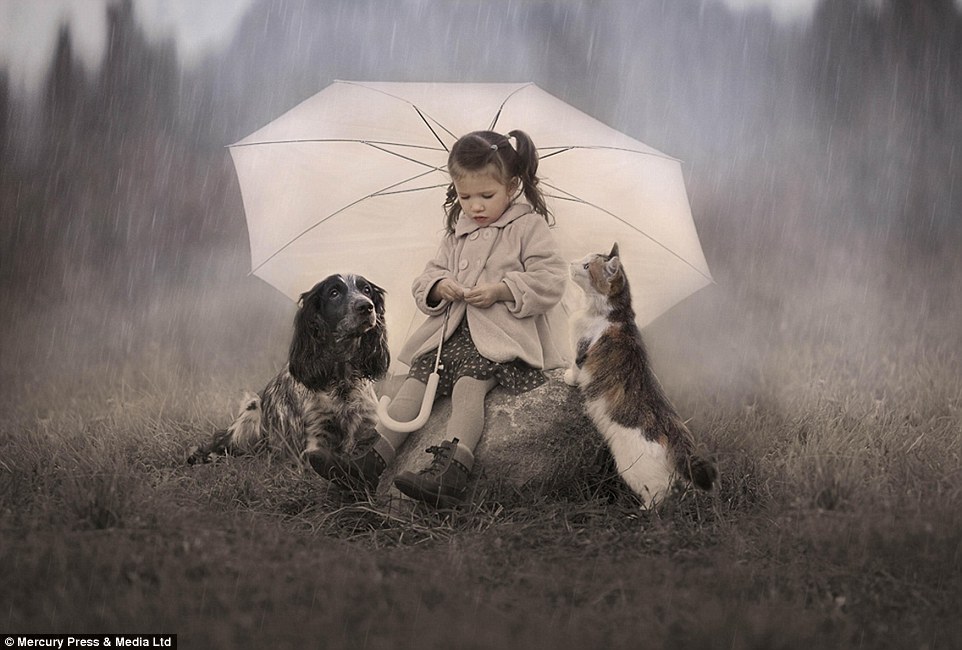 A girl shelters under the lashing rain on a rock with her spaniel and cat also jostling for a dry spot under her umbrella&nbsp;