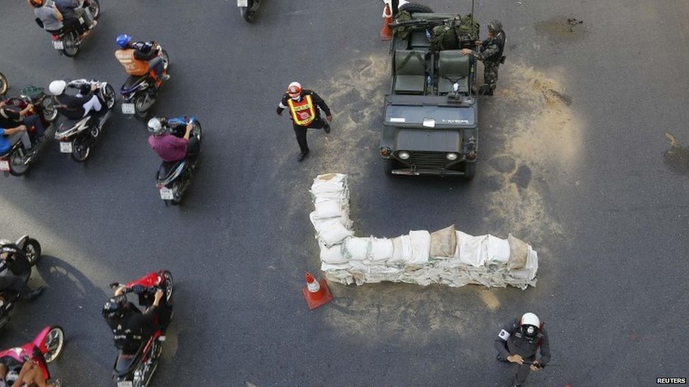 Commuters drive their motorcycles past Thai soldiers positioned in the middle of a main intersection in Bangkoks shopping district