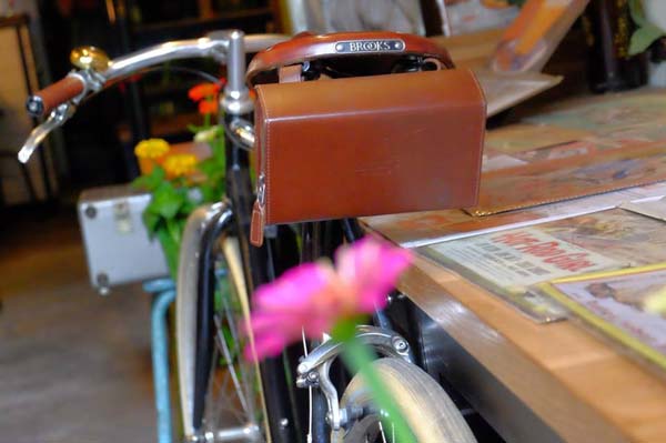 Một chiếc xe đạp cổ dựng b&ecirc;n cạnh chiếc b&agrave;n c&oacute; nhiều b&aacute;o v&agrave; tạp ch&iacute; cũ