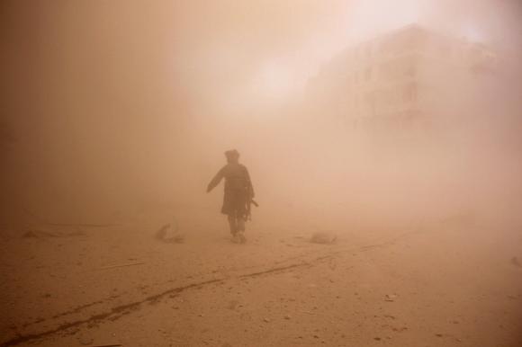 Một phiến quân nổi dậy Syria băng qua khu vực vừa bị ném bom ở TP Aleppo. Ảnh: Reuters