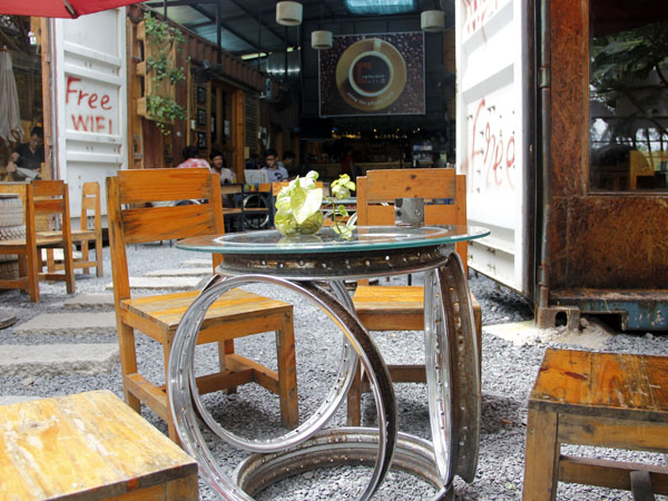 C&ugrave;ng với b&agrave;n ghế gỗ thường thấy, Caf&eacute; Contaier c&ograve;n tận dụng những phụ t&ugrave;ng bỏ đi của m&ocirc; t&ocirc;, xe hơi, xe tải như vỏ xe, m&acirc;m, s&ecirc;n cam, v&ograve;ng bi, bạc đạn... l&agrave;m th&agrave;nh những đồ trang tr&iacute; nhằm g&acirc;y ấn tượng cho kh&aacute;ch, cũng như tạo phong c&aacute;ch bụi bậm của chủ nh&acirc;n.