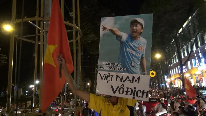 Người đ&agrave;n &ocirc;ng cầm tấm h&igrave;nh của HLV Miura, b&ecirc;n dưới c&oacute; d&ograve;ng chữ Việt Nam v&ocirc; địch