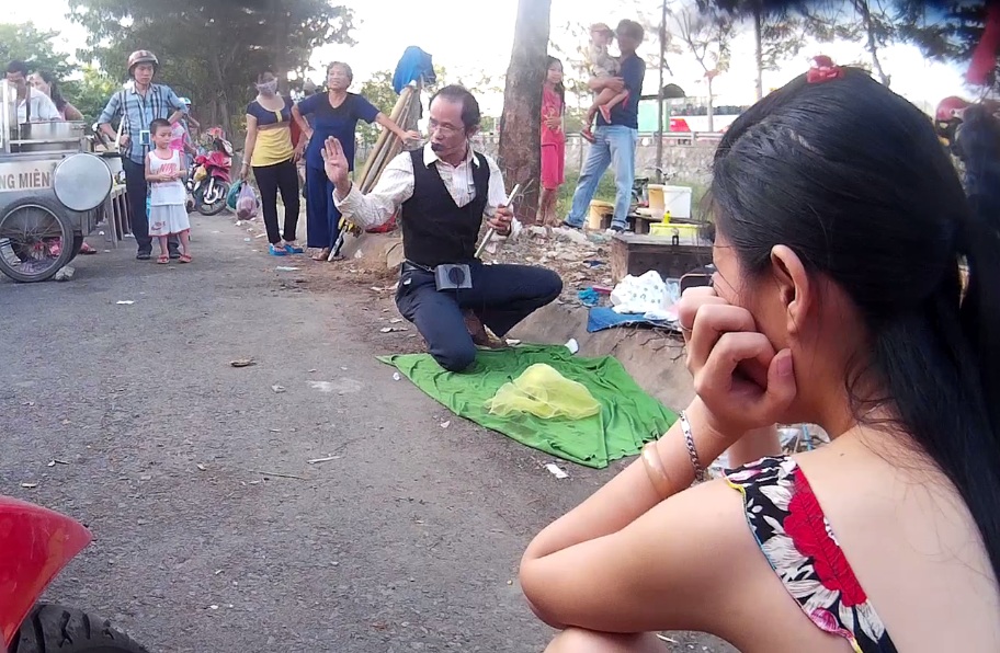 Gã đàn ông tự xư là Hoành Phi Thanh, người con trai út của nhà thuốc gia truyền Thiện Chí đang trình diễn ảo thuật miễn phí.