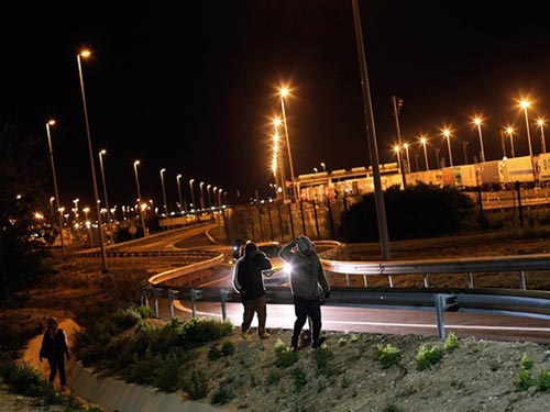 Người di cư đi bộ bên ngoài khu vực do Eurotunnel quản lý ở TP Calais - Pháp đêm 28-7 Ảnh: AP