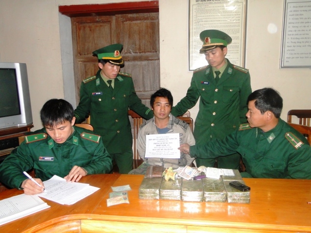Hạ B&aacute; Cu (giữa) c&ugrave;ng tang vật 20 b&aacute;nh heroin bị lực lượng Bộ đội Bi&ecirc;n ph&ograve;ng tỉnh Nghệ An bắt giữ  v&agrave;o ng&agrave;y 28-12-2014  Ảnh: Đức Ngọc
