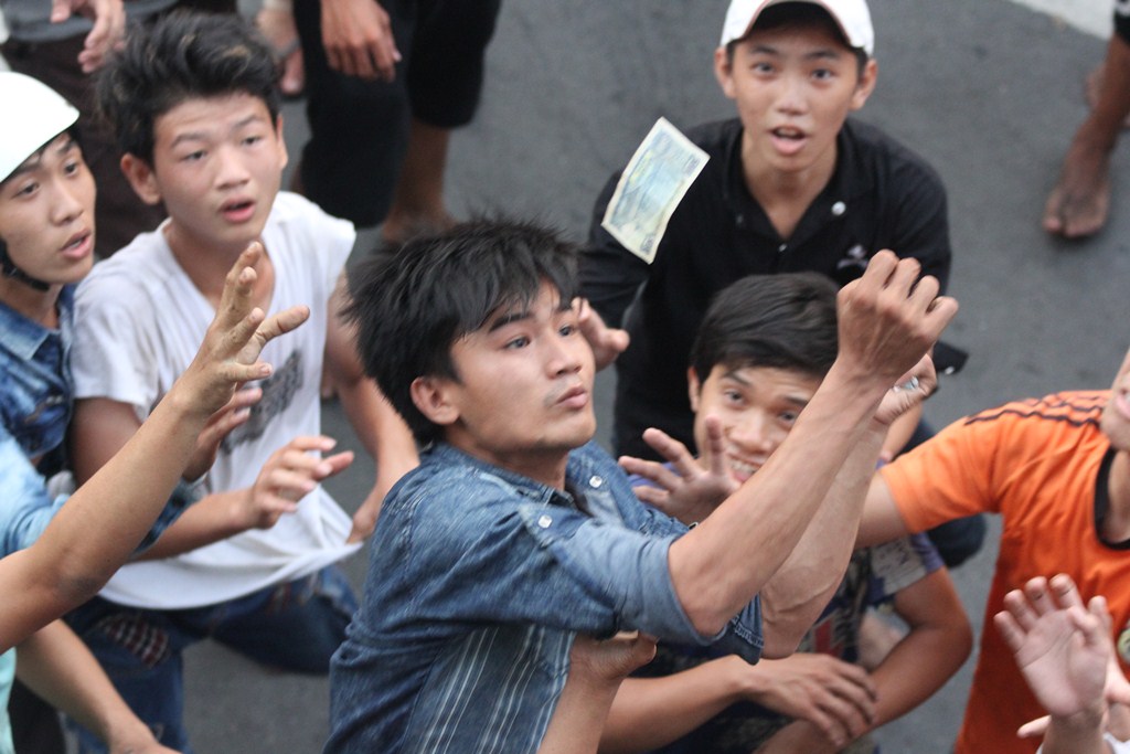 Gia chủ rải tiền lẻ từ tr&ecirc;n cao xuống. Ph&iacute;a dưới nhiều thanh ni&ecirc;n giẫm đạp, tranh nhau để nhận.