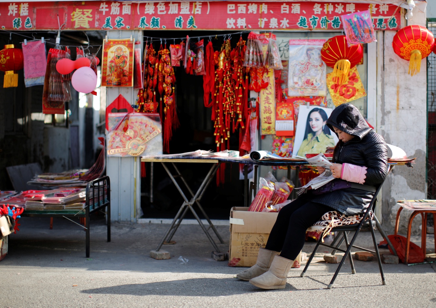 A vendor, selling traditional decorations for the upcoming Chinese Lunar New Year, reads a newspaper as she waits for customers at a migrant workers village in Beijing February 12, 2015. Photo by Kim Kyung-Hoon/REUTERS.