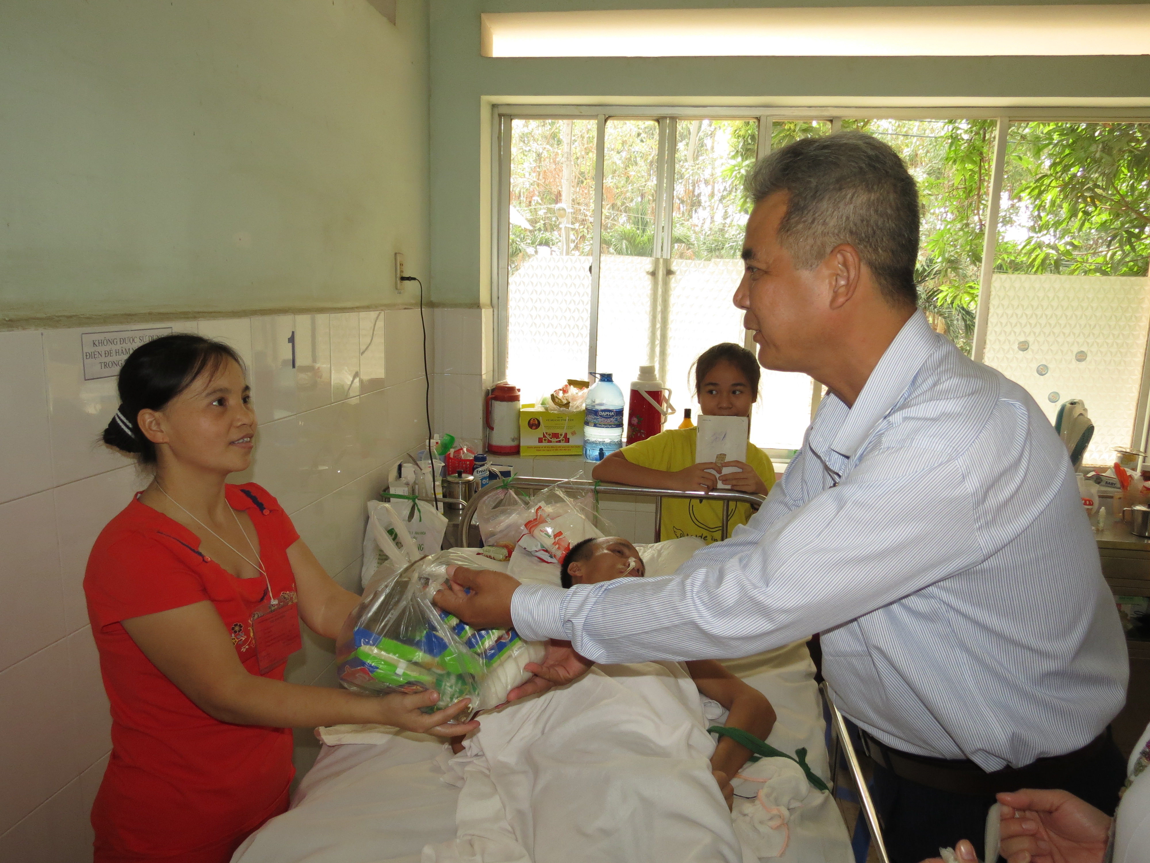 Nam bệnh nh&acirc;n n&agrave;y kh&ocirc;ng thể tự ngồi dậy, người nh&agrave; vui vẻ đ&oacute;n phần qu&agrave; thay anh.
