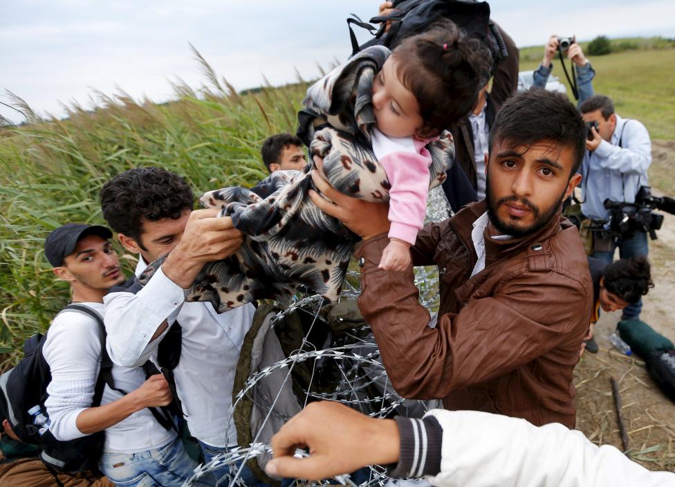 Một b&eacute; g&aacute;i được bế qua h&agrave;ng r&agrave;o d&acirc;y th&eacute;p gai ở bi&ecirc;n giới Hungary-Serbia. Ảnh: Reuters