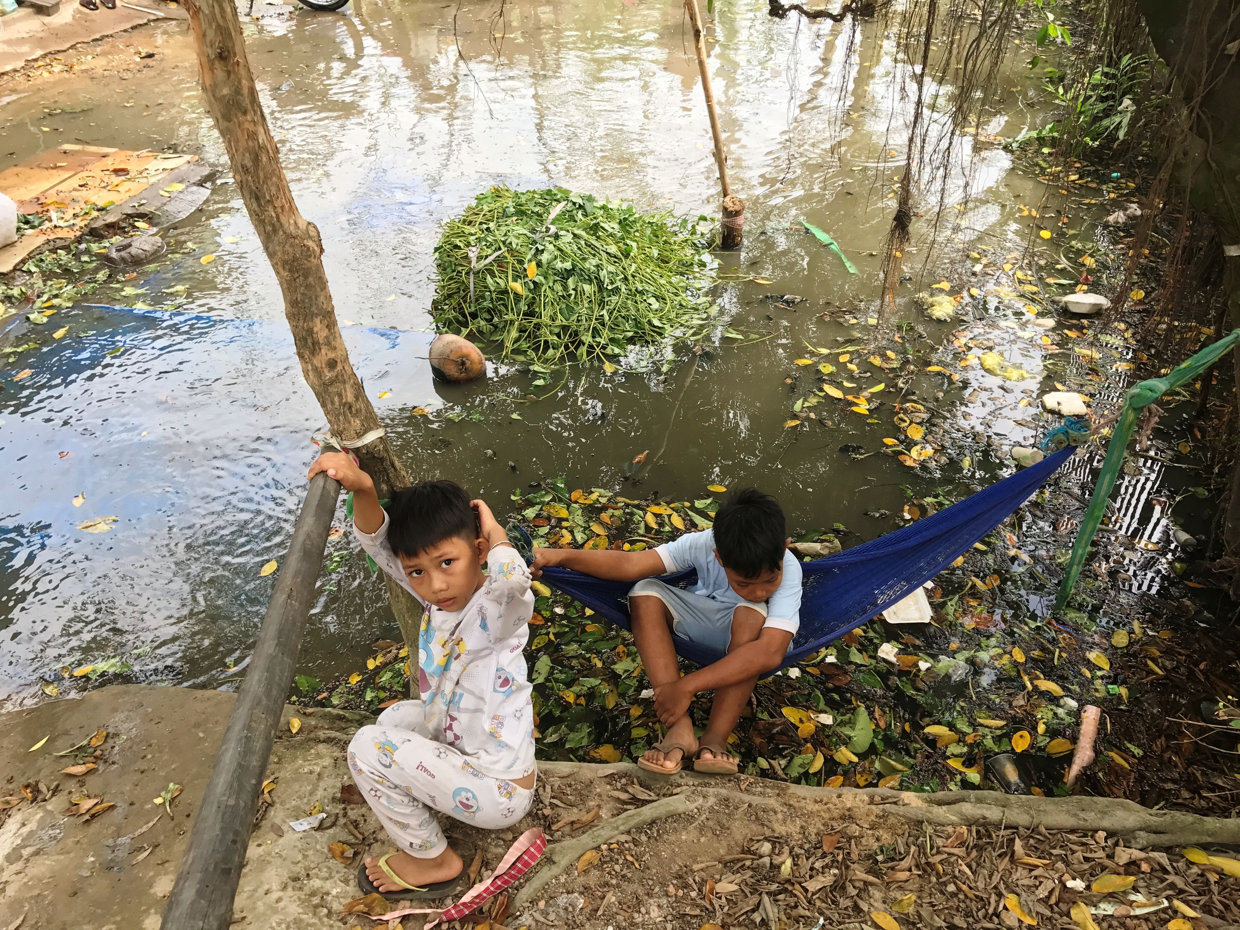 Hai em bé mắc võng trên đoạn đường bị nước ngập ngồi chơi
