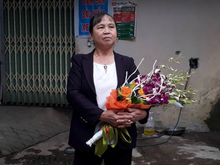 Một phụ nữ &ocirc;m hoa chờ đo&agrave;n đại biểu đến tặng