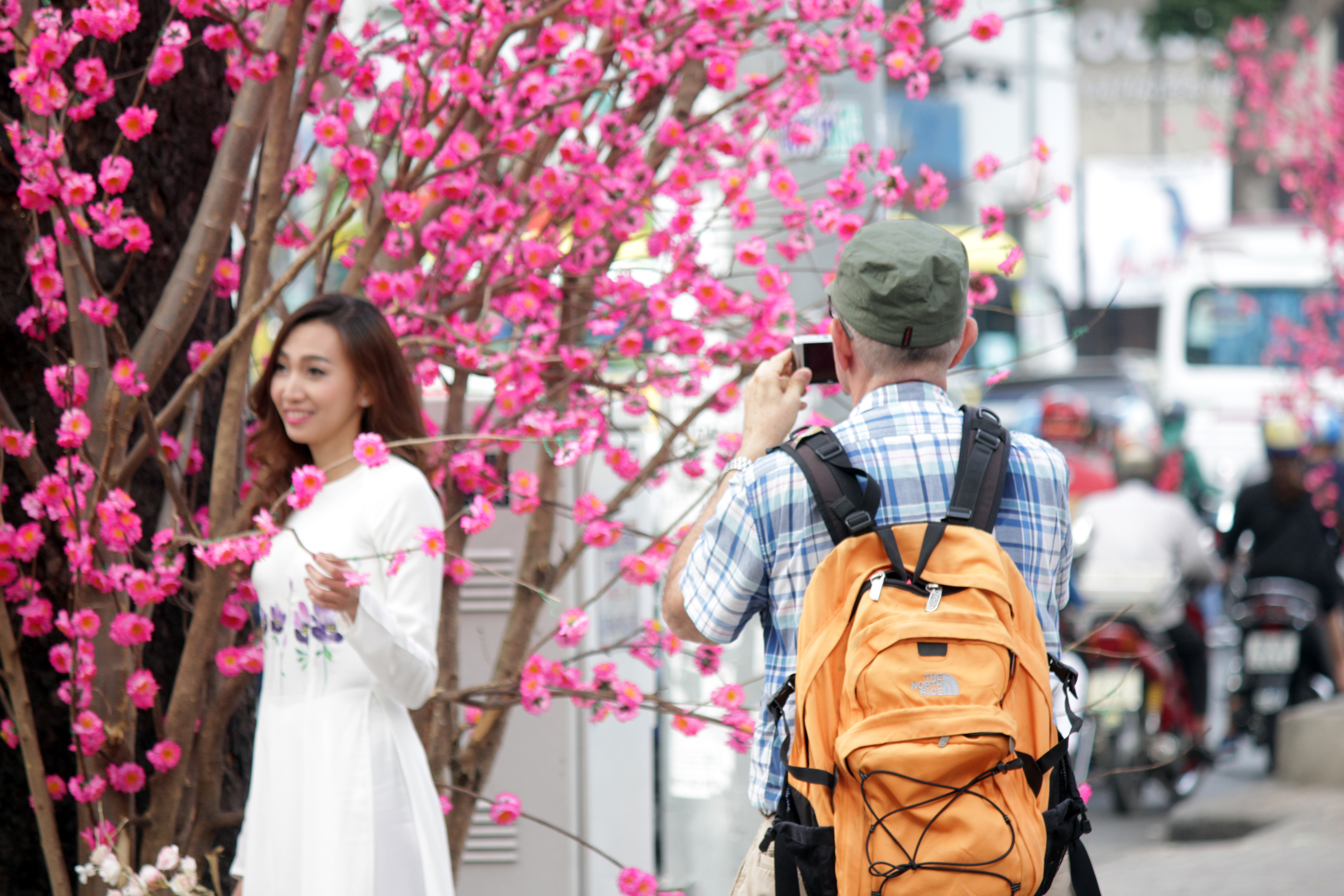 M&ocirc;̣t du khách nước ngoài thích thú ghi lại hình ảnh thi&ecirc;́u nữ mặc áo dài thướt tha tạo dáng b&ecirc;n hoa đào.