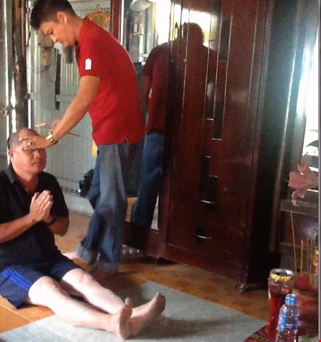 Người đàn ông áo đỏ vừa ấn tay vô trán và thái dương, vừa quơ bó nhang cháy đỏ trên đầu PV để trục... tà ma. Ảnh: HẢI NGỌC