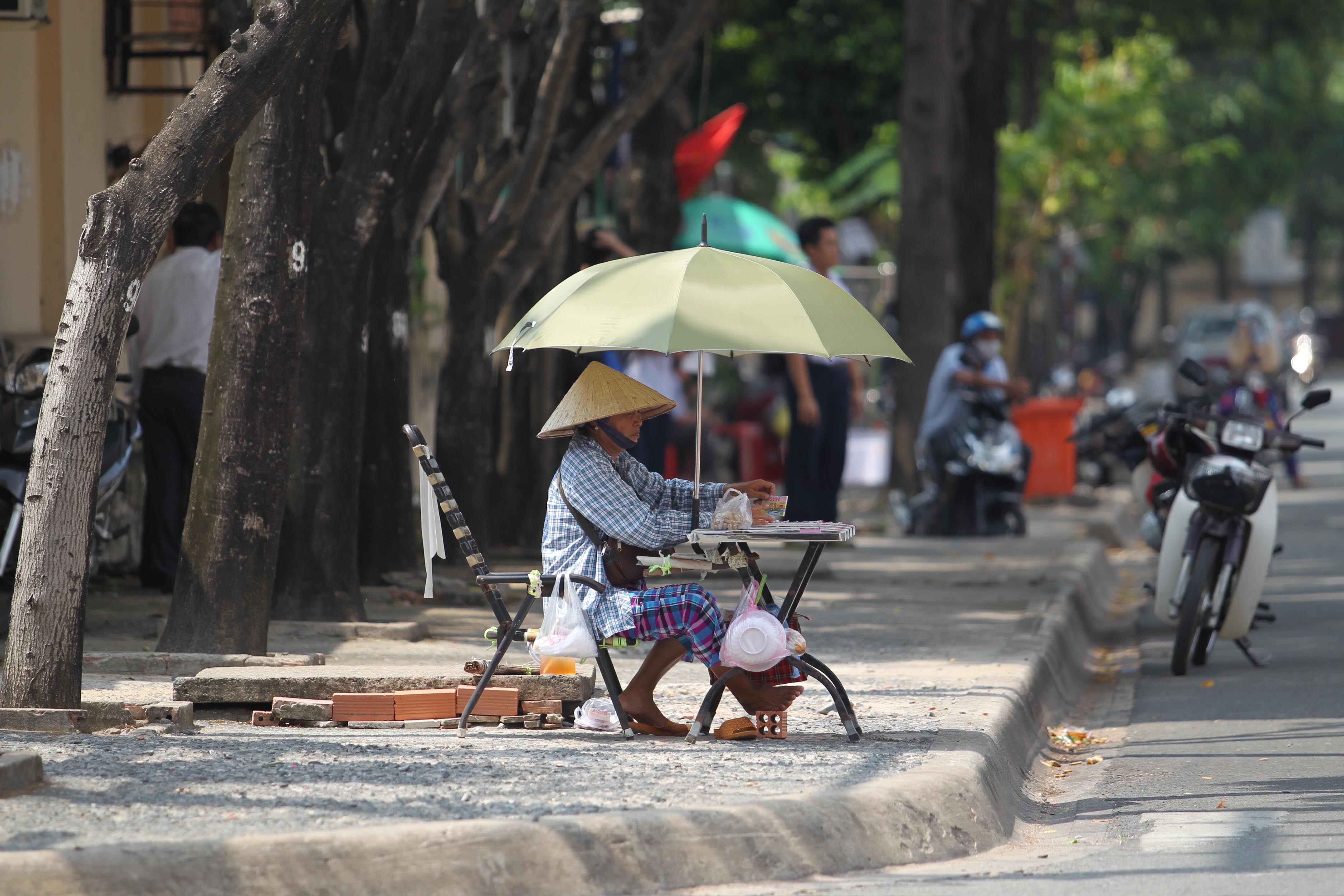 
Người phụ nữ b&aacute;n v&eacute; số d&ugrave; ngồi dưới t&aacute;n c&acirc;y nhưng vẫn che th&ecirc;m d&ugrave; để tr&aacute;nh nắng. C&ocirc; cho biết những người l&agrave;m nghề như c&ocirc; d&ugrave; trời nắng n&oacute;ng cỡ n&agrave;o cũng phải ra đường bu&ocirc;n b&aacute;n, nếu ở nh&agrave; sẽ kh&ocirc;ng c&oacute; tiền trang trải. Những ng&agrave;y qua, cứ về đến nh&agrave; l&agrave; người c&ocirc; như cọng b&uacute;n thiu.
