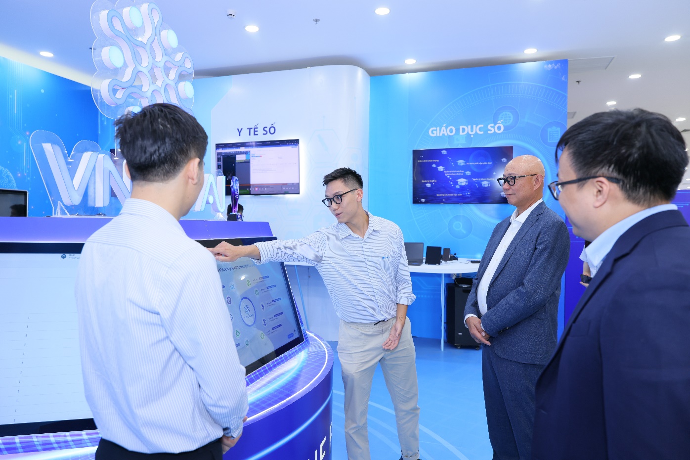 A group of men standing in front of a computer screen Description automatically generated