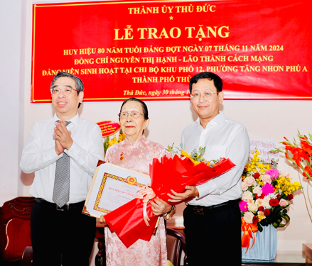 Ông Nguyễn Phước Lộc (bìa trái) cùng ông Trần Quốc Trung, Phó Bí thư Thường trực Thành ủy TP Thủ Đức, trao Huy hiệu 80 năm tuổi Đảng và tặng hoa chúc mừng đảng viên Nguyễn Thị Hạnh