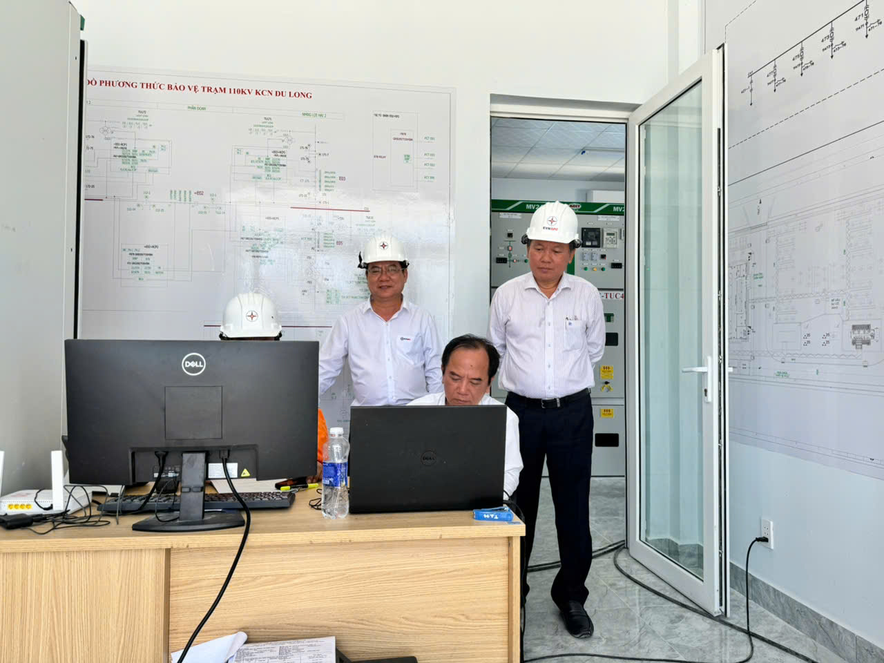 A group of men in hardhats standing in front of a computer Description automatically generated