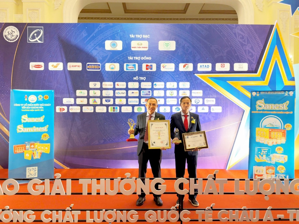 Two men holding awards on a stage  Description automatically generated