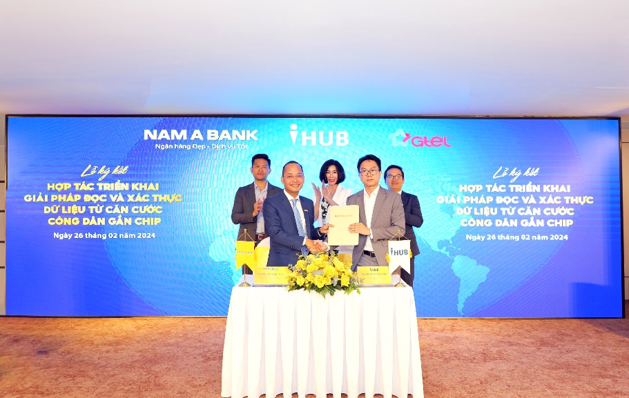 A group of people standing at a table with a table with flowers and a sign Description automatically generated