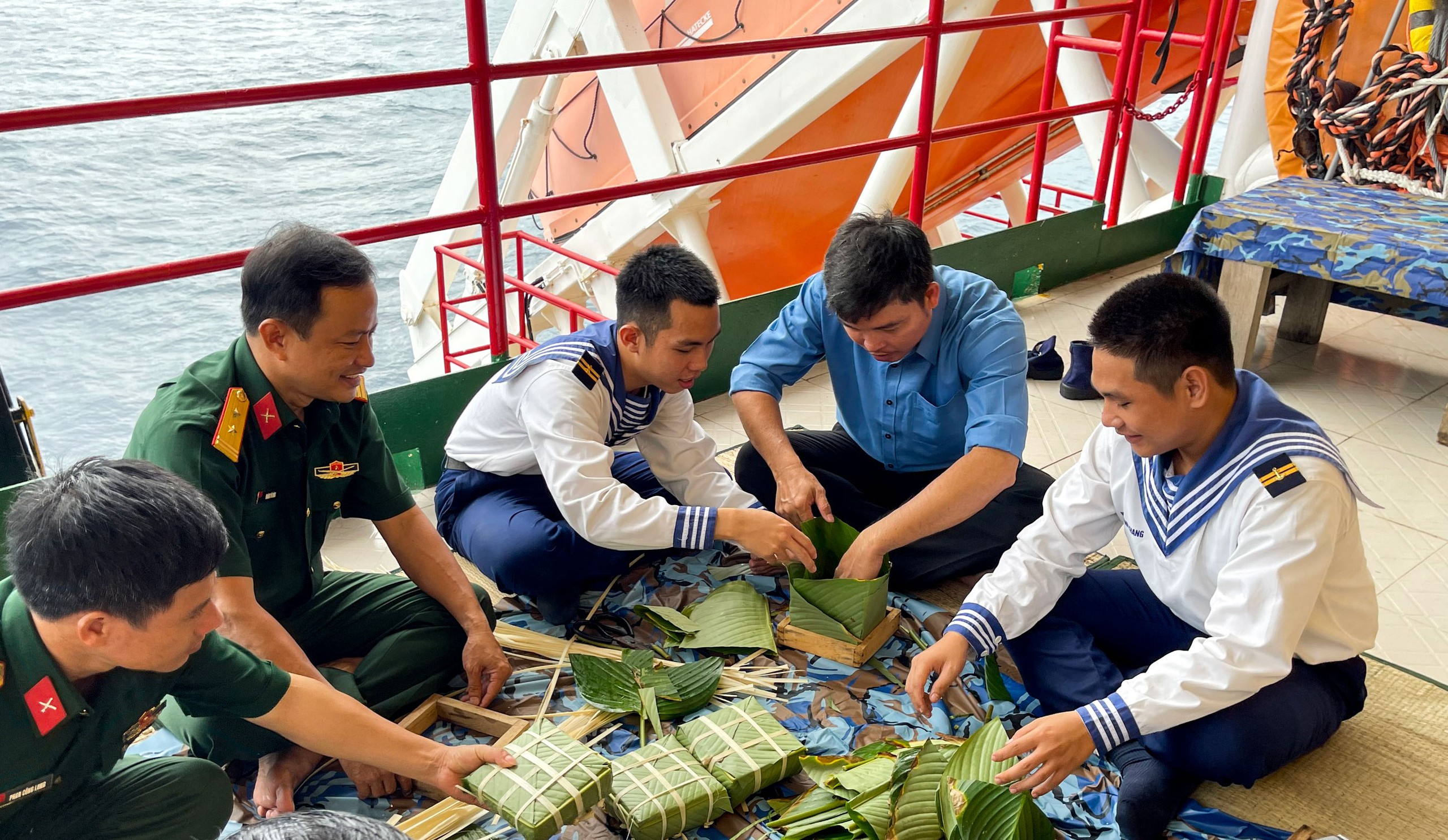Cán bộ, chiến sĩ nhà giàn DK1 gói bánh chưng. Trung sĩ Nguyễn Hoàng Tuấn Kiệt (thứ 3 từ phải sang) cho biết dù ở giữa biển khơi nhưng năm nào cán bộ, chiến sĩ nơi đây cũng được các đoàn công tác tặng gạo nếp, lá dong… để gói bánh chưng Ảnh: HỒNG QUÂN