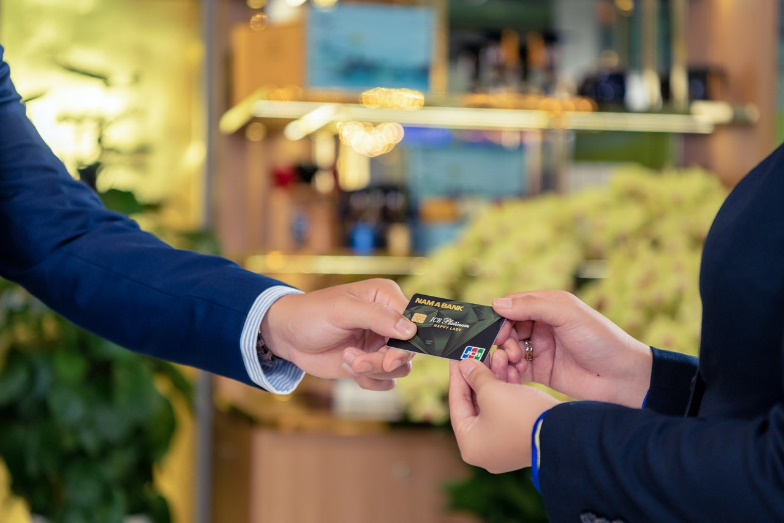 A person handing a credit card to another person Description automatically generated