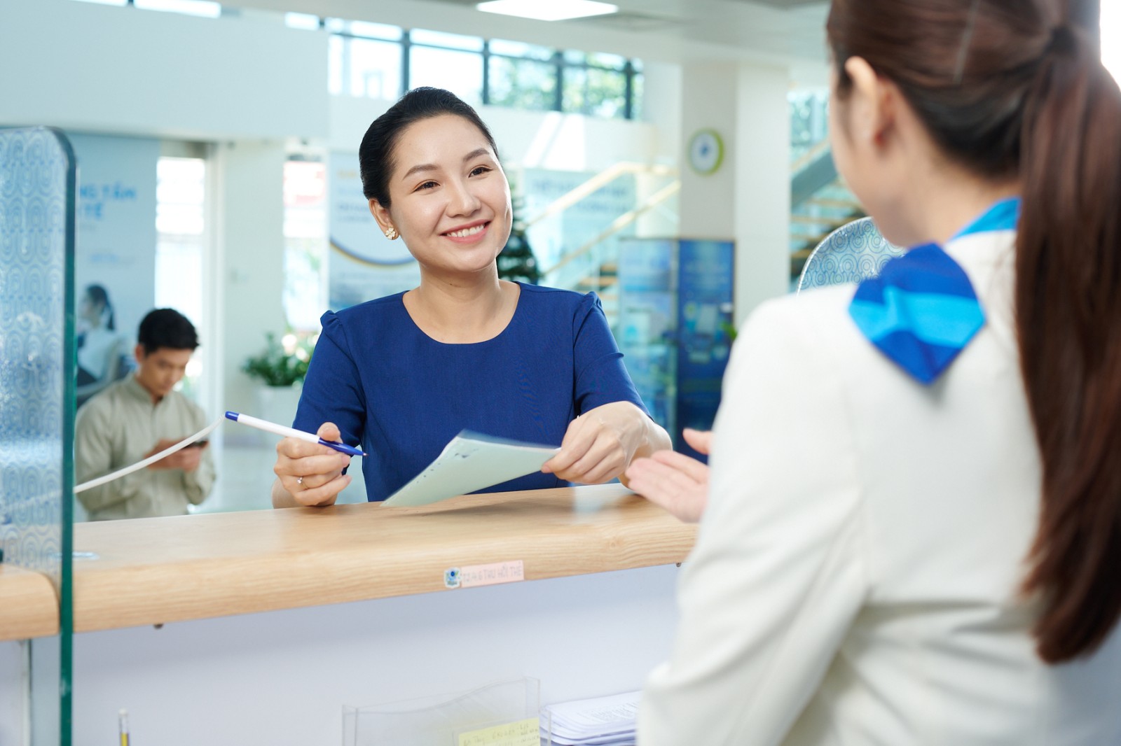 A person talking to a person at a reception desk  Description automatically generated