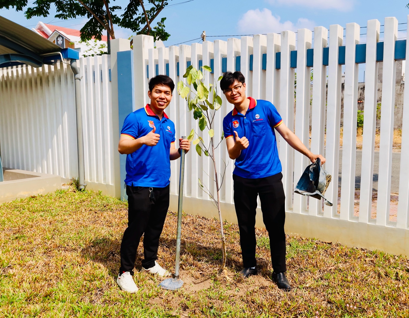 Two men in blue shirts holding a small tree Description automatically generated