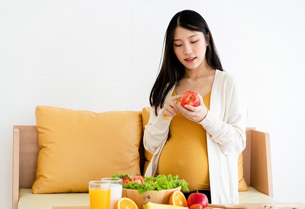 A pregnant person holding an apple Description automatically generated