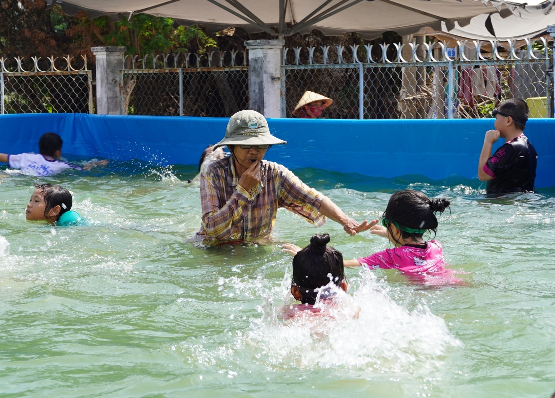 A person and children in a pool Description automatically generated