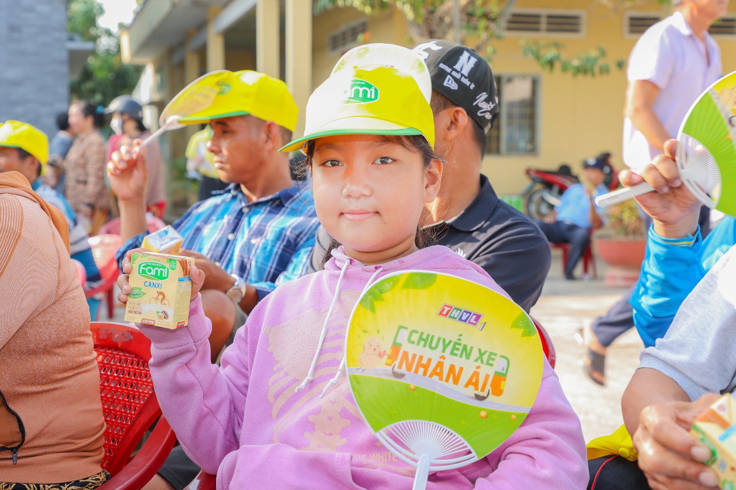 A child in a yellow hat holding a box and a fan  Description automatically generated