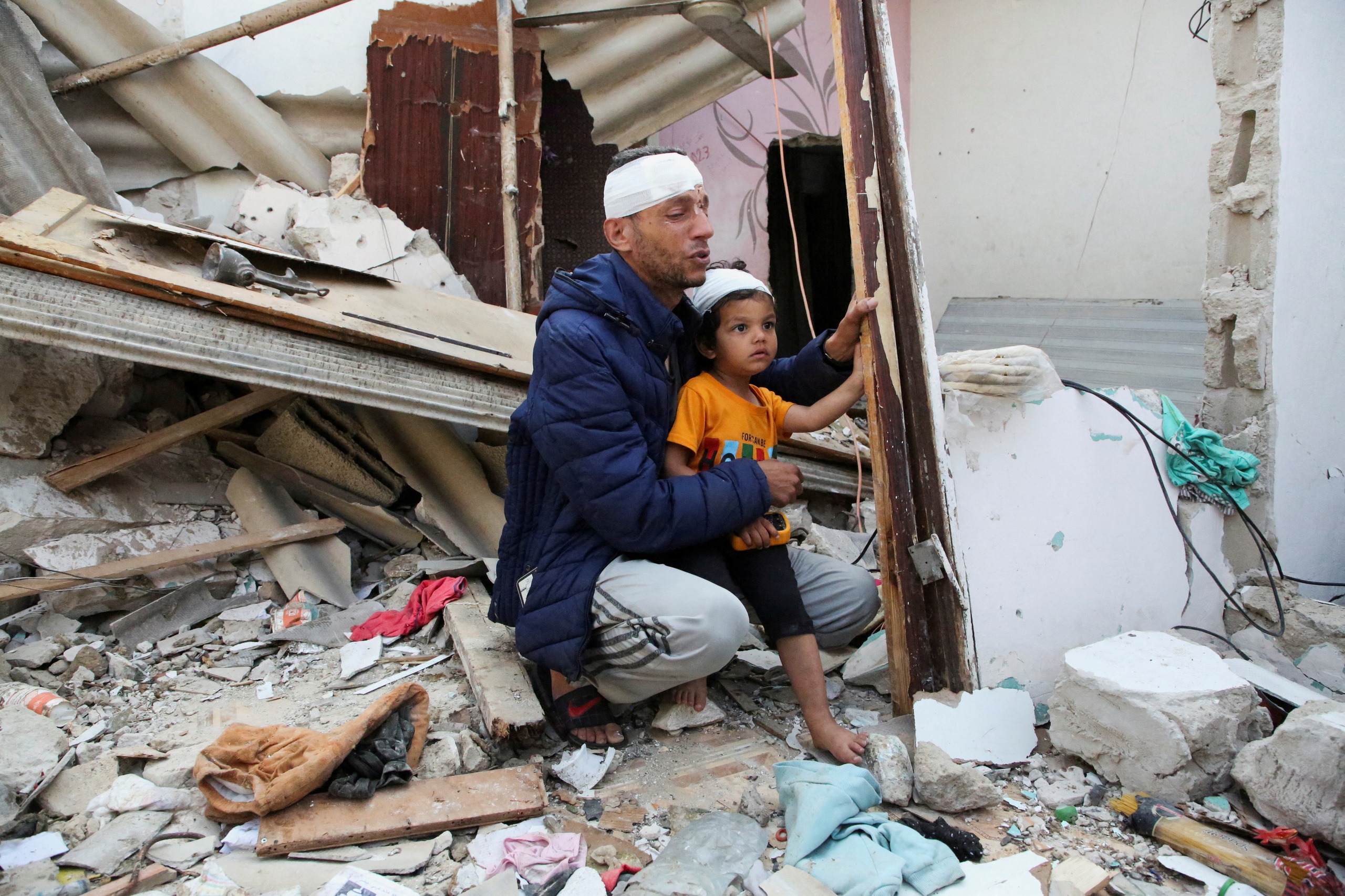 Hai cha con người Palestine bị thương ngồi trước một ng&ocirc;i nh&agrave; tr&uacute;ng kh&ocirc;ng k&iacute;ch của Israel ở Rafah, miền Nam Dải Gaza, h&ocirc;m 1-5 Ảnh: REUTERS