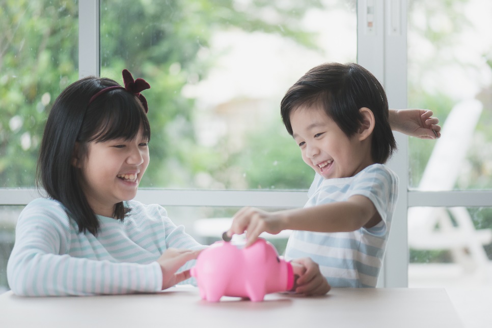 A child and child putting a coin into a piggy bank Description automatically generated