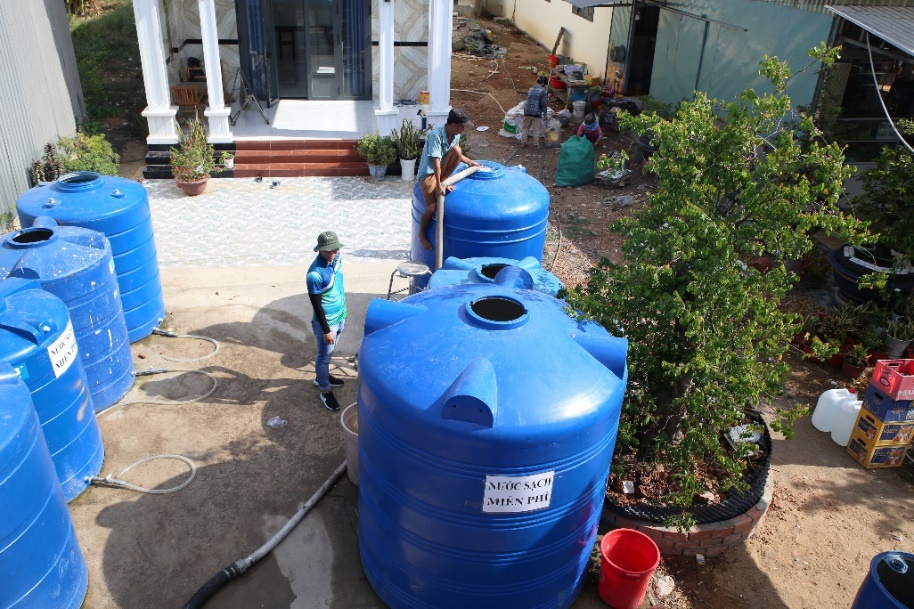 A group of people standing next to large blue tanks  Description automatically generated