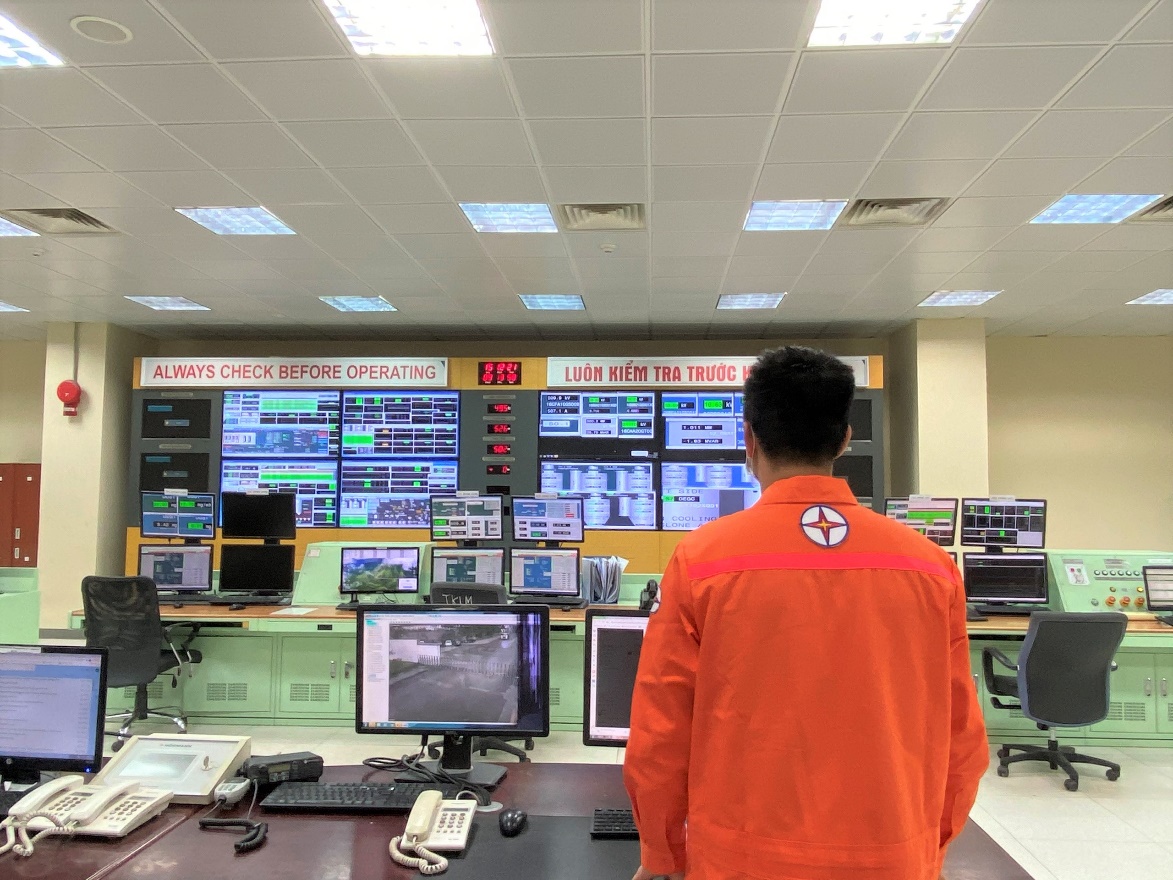 A person in an orange jumpsuit looking at a large screen Description automatically generated
