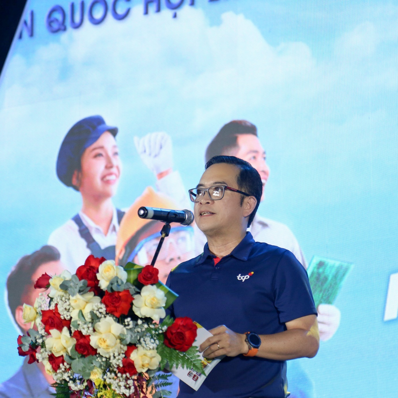 A person standing in front of a microphone with flowers Description automatically generated