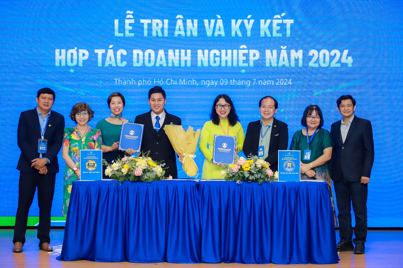 A group of people standing at a table with blue signs Description automatically generated