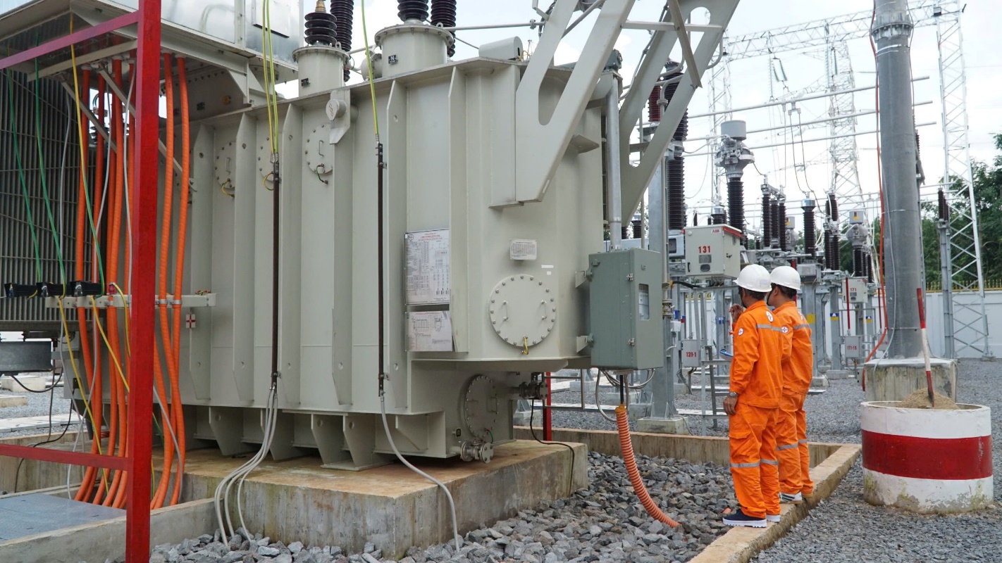 A group of men in orange jumpsuits standing next to a large machine Description automatically generated