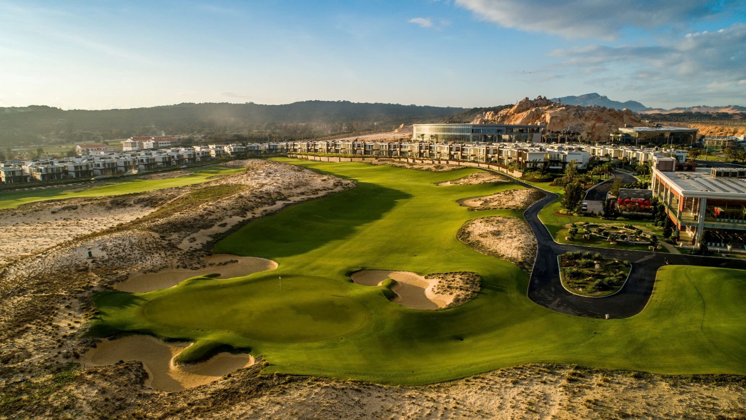 A golf course with a large green field and a building in the background Description automatically generated