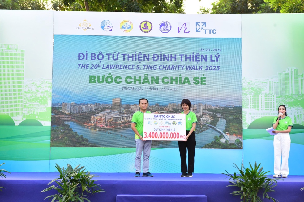 A person and person standing on a stage with a large sign Description automatically generated