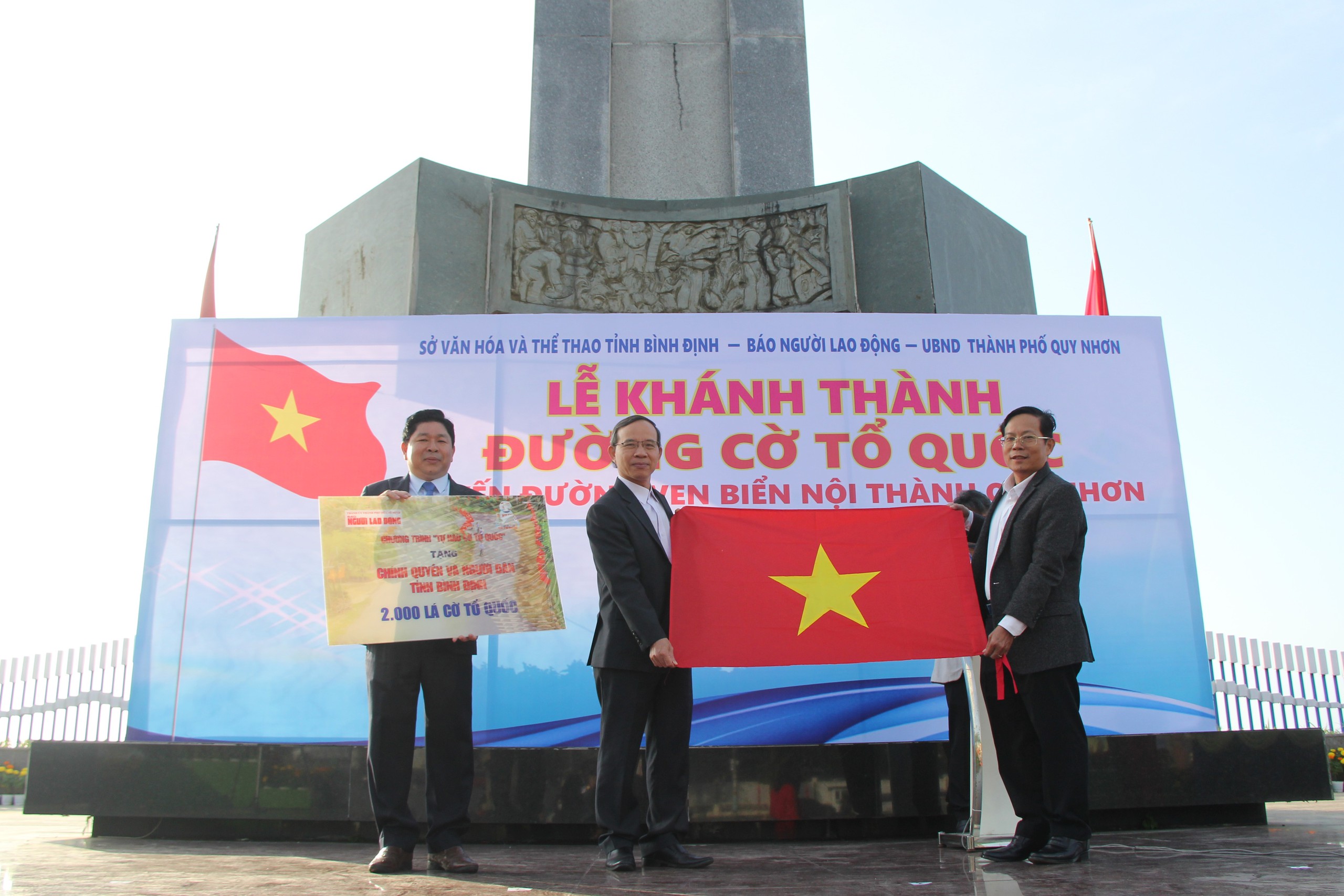 &Ocirc;ng T&ocirc; Đ&igrave;nh Tu&acirc;n, Tổng Bi&ecirc;n tập B&aacute;o Người Lao Động (b&igrave;a phải), trao tặng ch&iacute;nh quyền v&agrave; người d&acirc;n tỉnh B&igrave;nh Định 2.000  l&aacute; cờ Tổ quốc Ảnh: HẢI ĐỊNH
