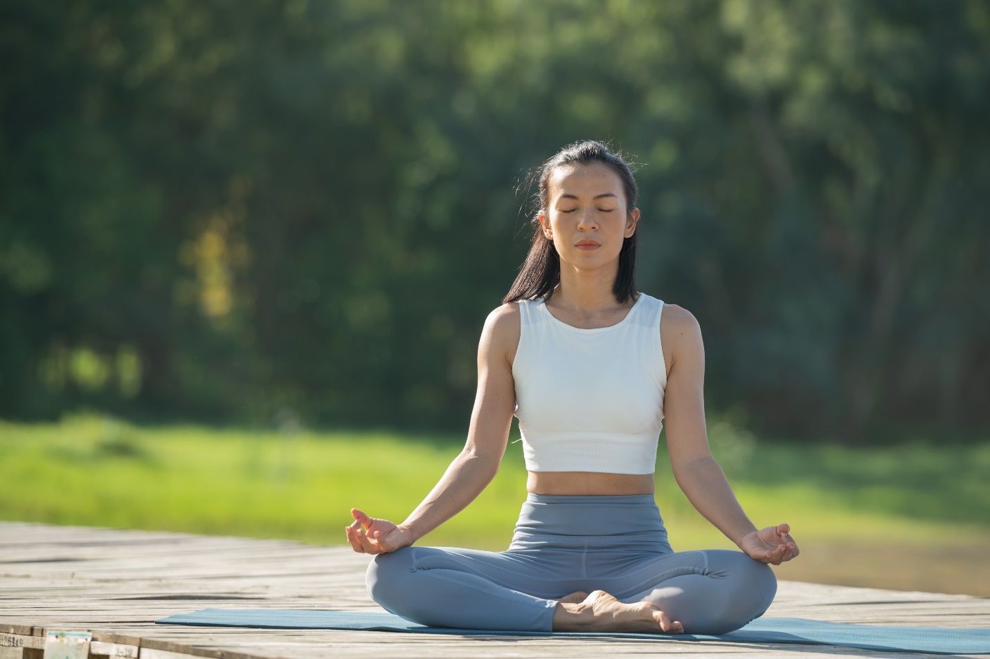 A person sitting cross legged on a mat with her eyes closed  Description automatically generated