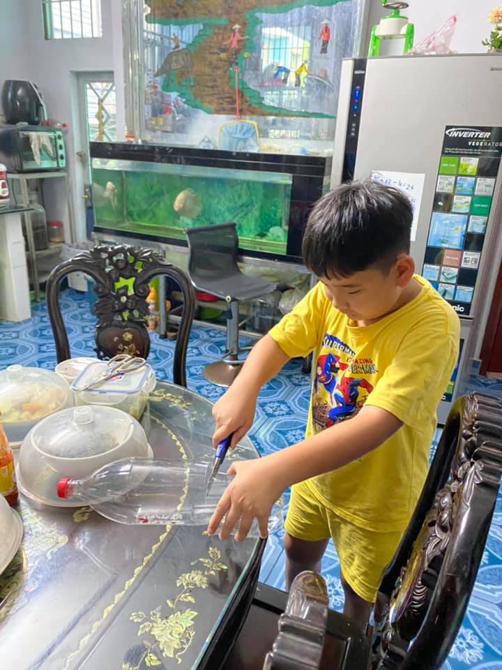 Nguyễn Đặng Gia Ph&uacute;c đang thực hiện l&agrave;m đồ đựng điện thoia5 v&agrave; ống cắm b&uacute;t từ chai nhựa đ&atilde; qua sử dụng. 