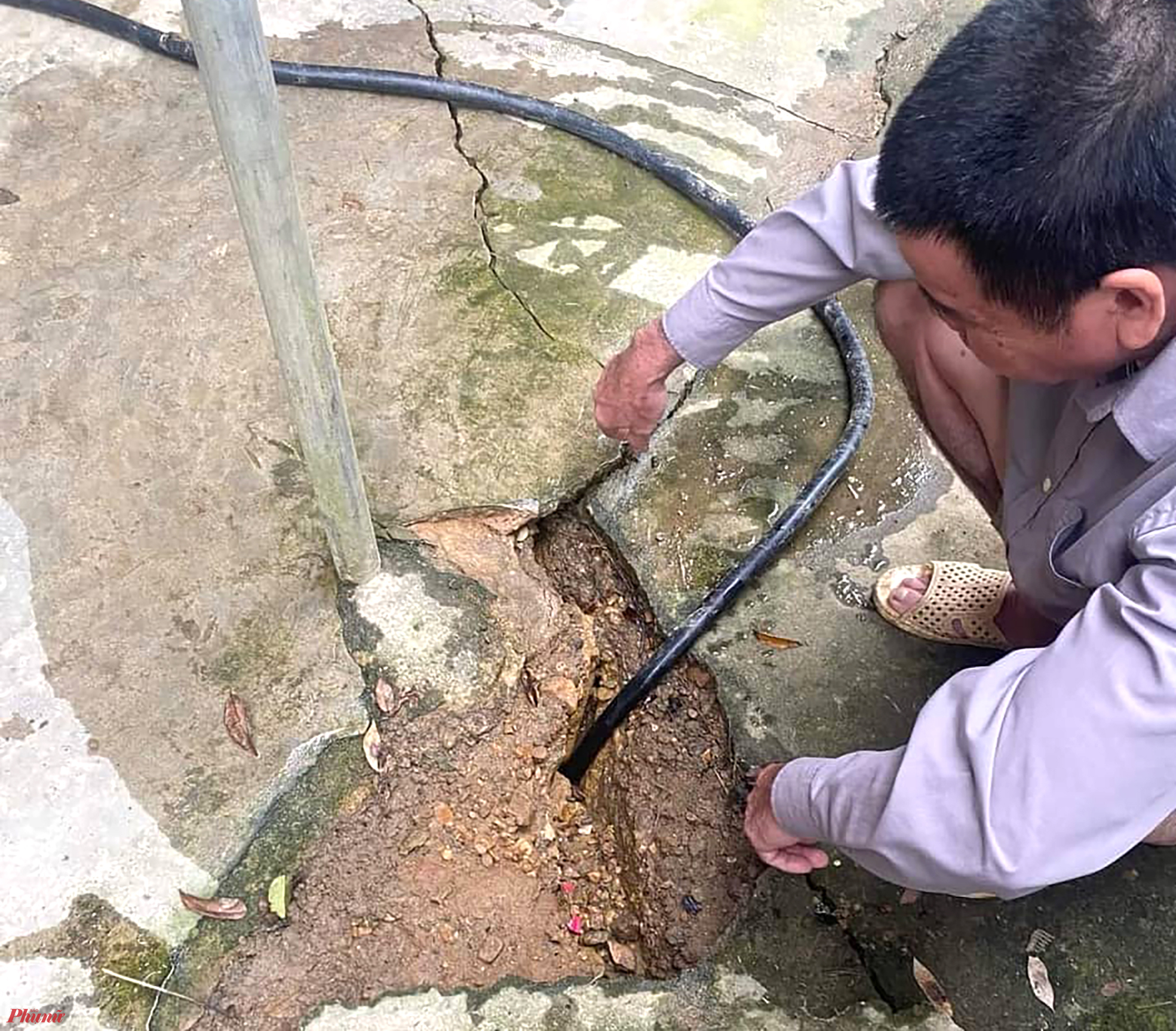Một người d&acirc;n x&atilde; Ch&acirc;u hồng d&ugrave;ng voi bơm nước v&agrave;o c&aacute;c vết nứt để kiểm tra độ s&acirc;u