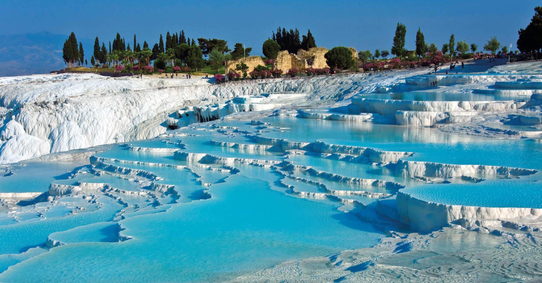 L&agrave; qu&ecirc; hương của miền t&acirc;y Thổ Nhĩ Kỳ, Pamukkale l&agrave; một khung cảnh si&ecirc;u thực với những bậc thang đ&aacute; v&ocirc;i trắng v&agrave; suối nước n&oacute;ng tự nhi&ecirc;n. Địa điểm tự nhi&ecirc;n n&agrave;y c&oacute; m&agrave;u trắng đặc biệt nhờ canxi được tạo ra bởi c&aacute;c suối nước n&oacute;ng, sau đ&oacute; h&oacute;a đ&aacute; v&agrave; sơn m&agrave;u trắng tại chỗ. Mọi người đ&atilde; tắm trong hồ bơi tự nhi&ecirc;n của n&oacute; trong h&agrave;ng ng&agrave;n năm. Th&agrave;nh phố cổ Hierapolis được x&acirc;y dựng tr&ecirc;n đỉnh Pamukkale, v&agrave; ng&agrave;y nay du kh&aacute;ch c&oacute; thể chứng kiến ​​sự đổ n&aacute;t của nh&agrave; tắm v&agrave; c&aacute;c di t&iacute;ch Hy Lạp kh&aacute;c tr&ecirc;n địa điểm n&agrave;y.