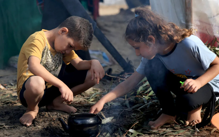 Những đứa trẻ Palestine di tản trong nước, những người chạy trốn khỏi cuộc bắn ph&aacute; của Israel ở ph&iacute;a bắc Gaza v&agrave; hiện đang sống trong những nơi tr&uacute; ẩn tạm bợ, đốt lửa để đun ấm nước sau cơn mưa ở Khan Younis v&agrave;o ng&agrave;y 15 th&aacute;ng 11 năm 2023. [Mahmud Hams/AFP]