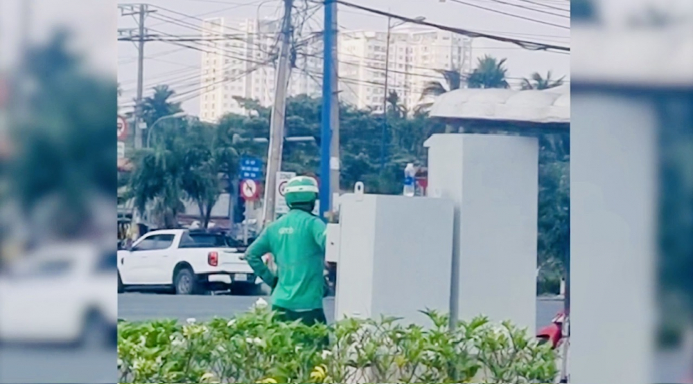 H&igrave;nh ảnh người đ&agrave;n &ocirc;ng mặc đồ GrabBike chỉnh t&iacute;n hiệu đ&egrave;n giao th&ocirc;ng ở TP Thủ Đức