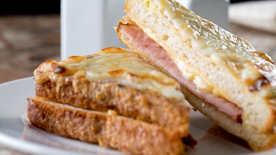 Croque-monsieur Theo Larousse, loại b&aacute;nh sandwich n&oacute;ng cổ điển của Ph&aacute;p n&agrave;y bao gồm một l&aacute;t giăm b&ocirc;ng mỏng v&agrave; ph&ocirc; mai tan chảy kẹp giữa hai l&aacute;t b&aacute;nh m&igrave;. M&oacute;n đầu ti&ecirc;n xuất hiện tr&ecirc;n thực đơn của người Paris v&agrave;o năm 1910, v&agrave; một số người cho rằng n&oacute; được ph&aacute;t minh ra một c&aacute;ch t&igrave;nh cờ, khi những c&ocirc;ng nh&acirc;n Ph&aacute;p để bữa trưa của họ gần một l&ograve; sưởi n&oacute;ng, chỉ để quay lại sau đ&oacute; v&agrave; ph&aacute;t hiện ra rằng ph&ocirc; mai trong b&aacute;nh sandwich của họ đ&atilde; tan chảy.  Nếu bạn muốn nếm thử một chiếc croque đ&iacute;ch thực, ph&ocirc; mai phải l&agrave; Gruyere (trộn với bechamel để c&oacute; được nước sốt Mornay) v&agrave; to&agrave;n bộ chiếc b&aacute;nh sandwich phải được x&agrave;o trong bơ cho đến khi gi&ograve;n v&agrave; c&oacute; m&agrave;u v&agrave;ng n&acirc;u. Croque-monsieur rất phổ biến đến nỗi tiểu thuyết gia nổi tiếng Proust thậm ch&iacute; đ&atilde; viết về n&oacute; trong kiệt t&aacute;c năm 1918 của &ocirc;ng l&agrave; In Search of Lost Time . 